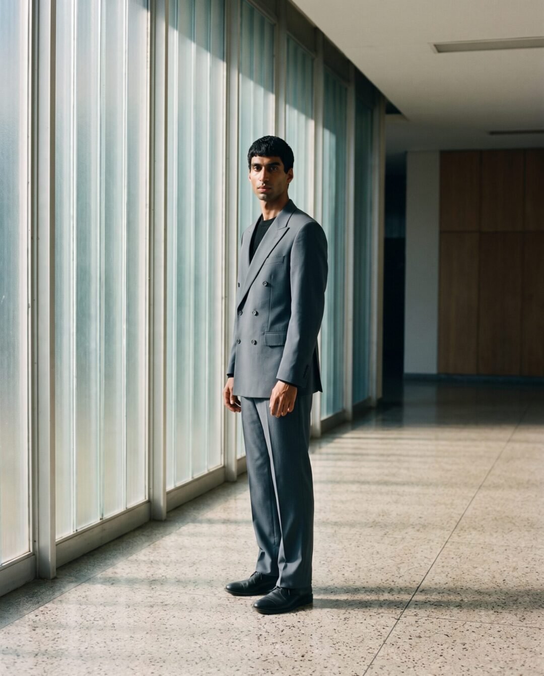 Ethan Naidoo in a slate suit in a modernist lobby