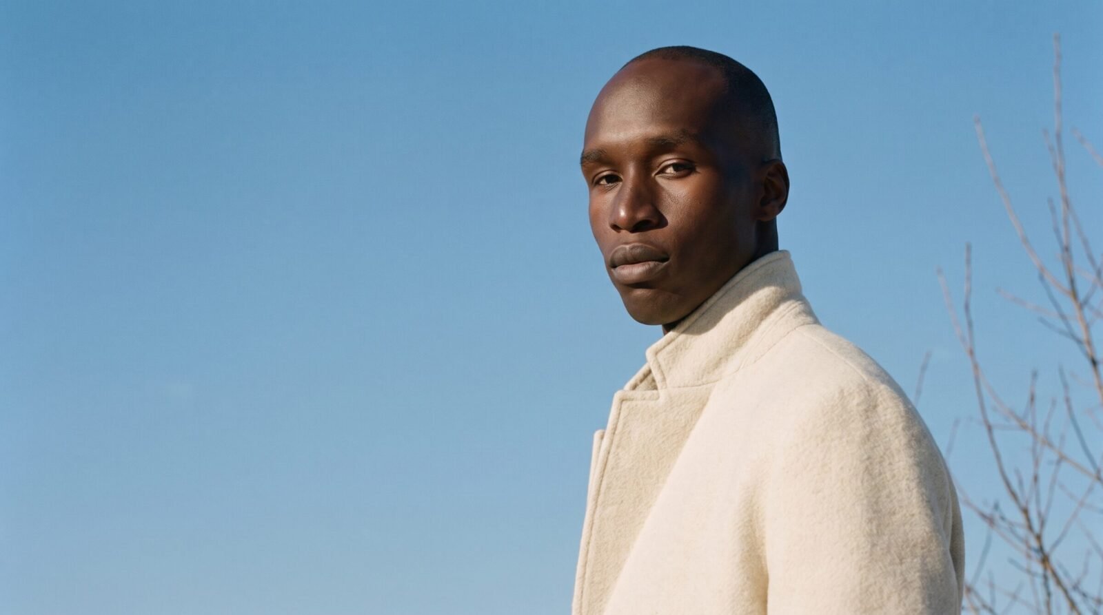 Kagiso Molefe in a cream high-collar coat against a winter sky